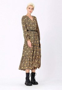 Robe midi à manches longues, avec un motif noir et jaune, décolletée en V et ceinturée d'une ceinture élastiquée noire. Associée à des bottes noires à lacets.