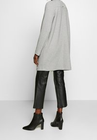 Šedý svetr s dlouhým rukávem a texturovaným pletením, doplněný o černé kožené kalhoty s krátkou délkou a kotníkové boty na podpatku s hladkým povrchem.