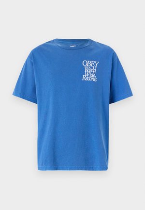 Blå bomull t-skjorte med korte ermer, rund hals, og hvit grafisk tekst "OBEY World Wide Records" på venstre brystområde.