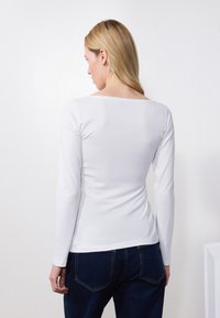 Top blanco de manga larga con escote cuadrado y textura suave. Combinado con jeans azul oscuro que presentan bolsillos estándar y costuras.