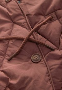 Pikowana, ocieplana kurtka w stonowanym mauve z plecionym sznurkiem do regulacji i brązowym guzikiem z czterema otworami do zapięcia. Gładka tekstura, nowoczesny design.