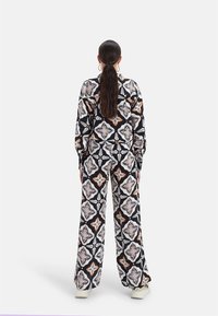 Conjunto negro de estampado que consiste en una camisa y pantalones de pierna ancha con intrincados diseños florales en tonos naranjas, blancos y morados.