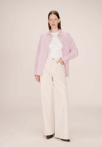 Camicia a righe rosa con bottoni sopra una t-shirt bianca, abbinata a pantaloni beige a gamba ampia e scarpe nere. Tessuto morbido e vestibilità rilassata.