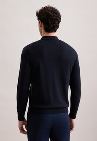 Granatowy polar z kołnierzykiem polo, długimi rękawami i ściągaczami. Posiada gładką teksturę i dopasowany krój.