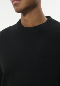 Czarny sweter z prążkowanym okrągłym dekoltem, wykonany z miękkiego, teksturowanego materiału, o dopasowanym kroju i minimalnych detalach.