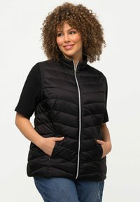 Svart pufferväst med hög krage, dragkedja framtill och horisontell quiltning. Har två sidofickor och kontrasterande material vid ärmarna.