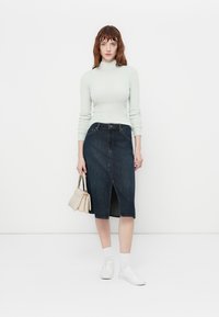 Lys grønn, ribbet langermet topp og mørk denim blyantskjørt med frontsplitt. Fullført med hvite sneakers og en liten beige håndveske.