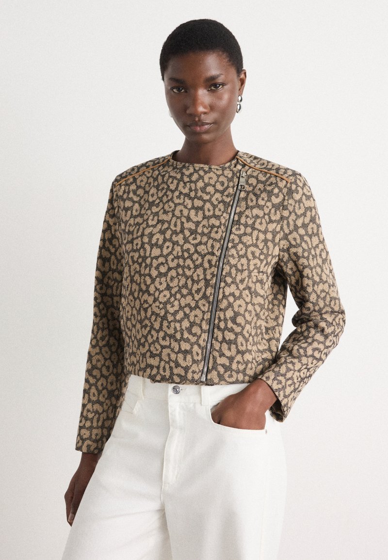 Korte jas met luipaardprint in beige en zwart stof, met een ritssluiting en gestructureerde schouders, gecombineerd met witte broeken.