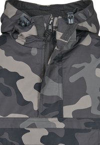 Svart og grå kamuflasje-pullover med høy krage, justerbare snorer og frontglidelås. Har glatt, vannavstøtende stoff.