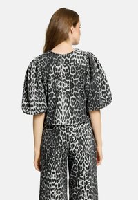Top a fantasia leopardata in bianco e nero, ritagliato, con maniche a palloncino, realizzato in tessuto testurizzato. Abbinato a pantaloni larghi a vita alta coordinati.