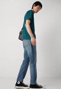 Teal cotton t-shirt, blue jeans, and black canvas high-top sneakers. Simple design with contrasting colors and relaxed fit. Accents include a small bag.
