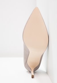 Beige High Heelschuh mit spitzer Zehe, strukturiertem Äußeren und schlankem Absatz. Die Sohle ist glatt und in heller Farbe.