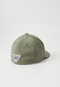 Cască verde din bumbac. Are o coroană rotundă, o vizieră curbată și un patch alb cu un logo triunghiular în spate. Sunt prezente șase găuri de ventilație.