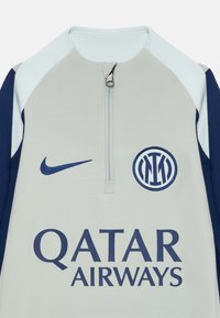 Nike zip-up hettegenser i lys grå og marineblå, med kvart-glidelås hals, laglogo og sponsor tekst i mørk blå foran.