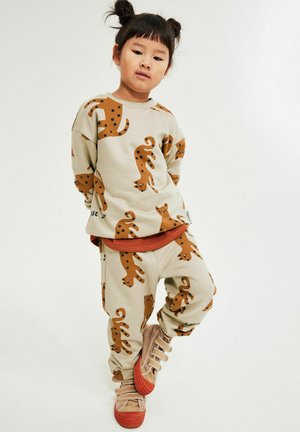 Brunligt sæt med brune og sorte katteprint; sweatshirt med lange ærmer, bukser med elastik i taljen; kombineret med beige sko.