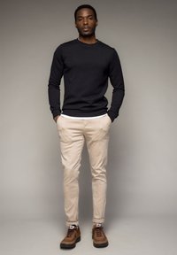 Maglietta nera a maniche lunghe, pantaloni slim-fit beige e sneaker marroni con lacci. Texture del tessuto liscia e design casual.