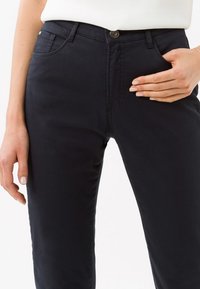 Pantaloni in cotone blu navy con un design aderente, tasche frontali e chiusura a bottone in vita. Texture liscia, dettagli minimi.