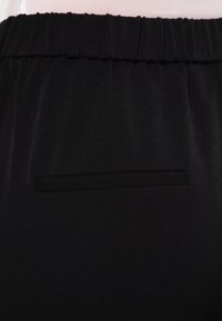 Svarta tygbyxor med en slät yta, med resår i midjan och en liten, diskret bakficka.