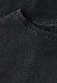 Nærbillede af en sort bomulds T-shirt halslinning, der viser fine ribbede detaljer og syninger.