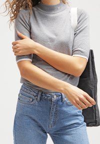 Grå kortärmad tröja med hög ribbad halsringning. Matchad med högmidjade blå denimjeans. Håller en svart tote-väska.