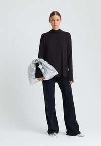 Haut noir à manches longues avec col montant, associé à un pantalon large bleu marine, tenant une veste en doudoune argentée. Des chaussures brillantes viennent compléter le look.