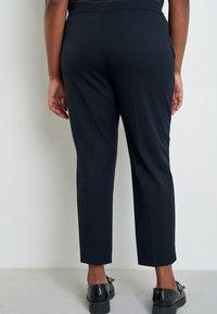 Marineblauwe cropped broek met een gestructureerde stof. Voorzien van een platte tailleband en rechte pijpen. Gekocht met zwarte schoenen, die de enkel tonen.