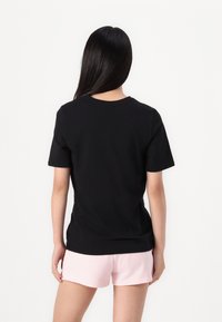 Black cotton t-shirt with a crew neck and short sleeves, paired with light pink shorts, viewed from the back, smooth texture.