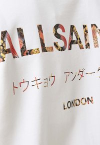 T-shirt bianco a maniche corte con stampa di lettere a serpente multicolore che spellano "ALLSAINTS" e "LONDON", con testo giapponese sottostante.
