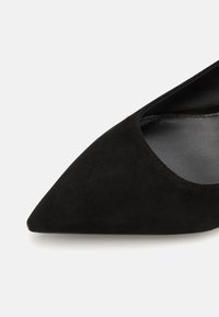 Scarpa nera in suede con punta affusolata, caratterizzata da una superficie liscia, lati tagliati bassi e un design elegante, con una fodera interna in contrasto.