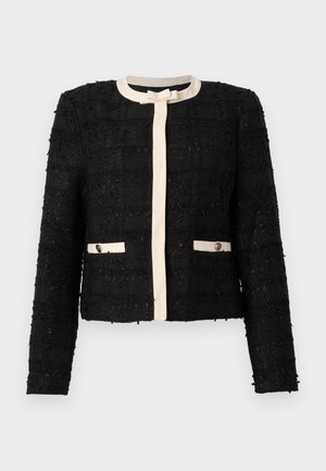 Svart tweedjakke med kremfarget kant, rund hals, lange ermer, sløyfedetalj foran og to kremkantede lommer med knapper.