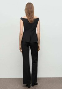 Zwarte op maat gemaakte top met off-shoulder ontwerp en flared broek. Het materiaal ziet er glad en aansluitend uit. Opmerkelijke details zijn een naad aan de achterkant.