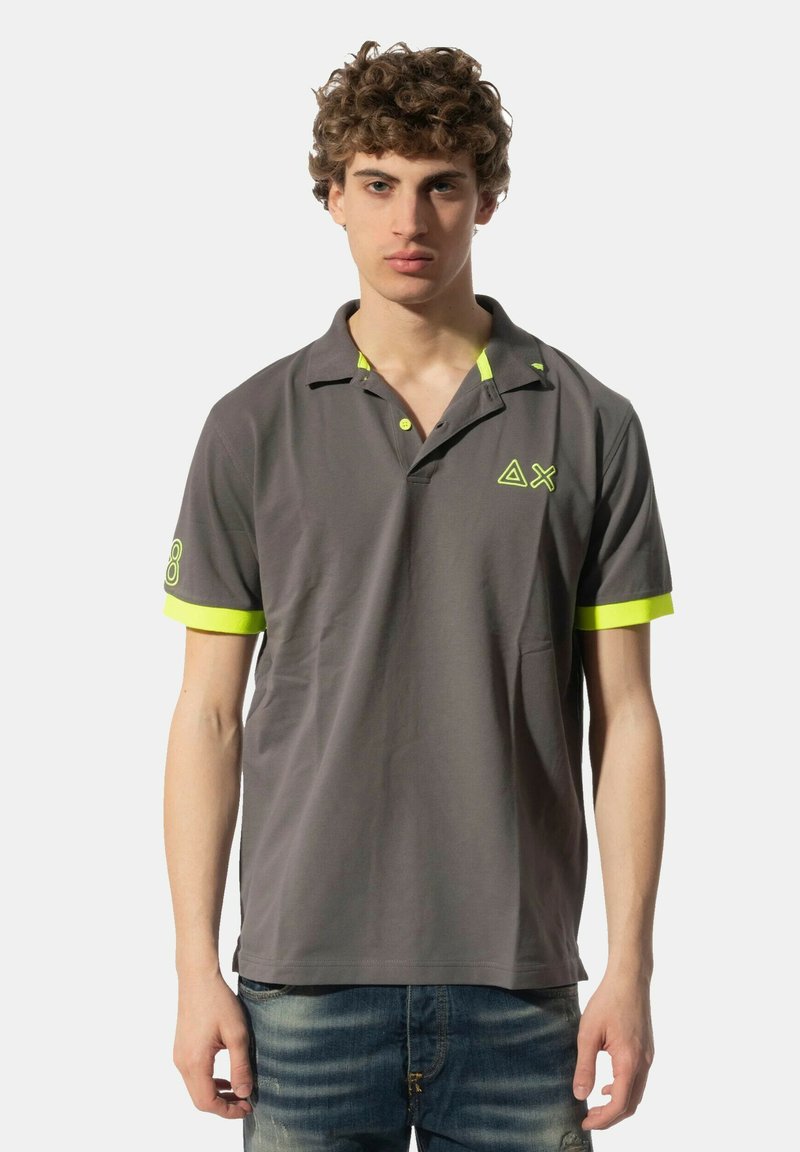 Polo grigio con accenti gialli sul colletto e sulle maniche, dotato di un logo sul lato sinistro del petto. Realizzato in un tessuto morbido.