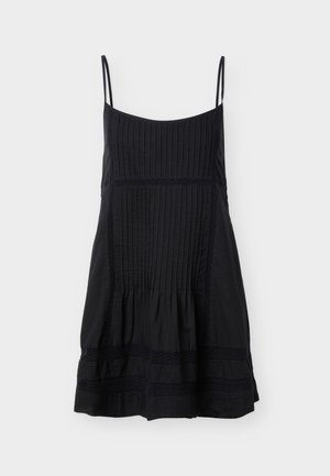 Svart ermeløs kjole med tynne stropper, vertikale folder på øvre og fremre paneler, og horisontale blondebånd nær kanten.