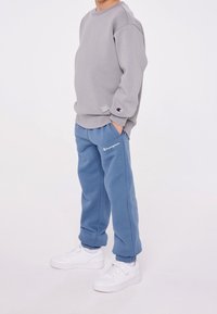 Felpa grigia con taglio classico e polsini a coste, abbinata a pantaloni della tuta in pile blu. Sneakers bianche completano l'outfit.