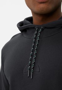 Felpa nera con tessuto texturizzato, cappuccio regolabile e lacci intrecciati neri e verdi con estremità in metallo. Dettaglio logo discreto.