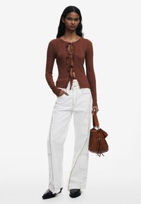 Ribbede rustfarvede sweater med frontknude, parret med hvide vidde bukser med kontrastsyninger og en brun håndtaske.