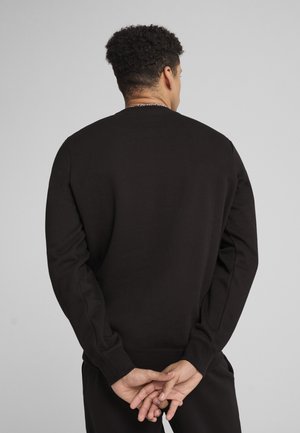 Hanorac negru dintr-un material moale, cu mâneci lungi, decolteu rotund și tiv elastic. Fără modele sau branding vizibil.