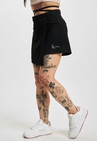 Svart omslagskjørt med knappelukking på siden og hvit logo-embroidery. Kombinert med hvite sneakers med lyse rosa detaljer.