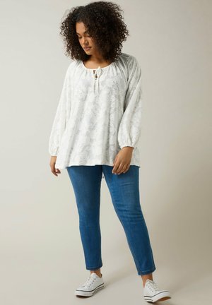 White floral textured blouse with long puff sleeves and keyhole neckline, paired with fitted blue jeans and white sneakers.