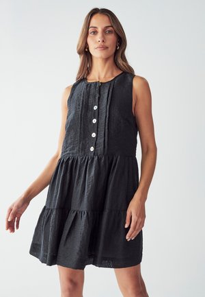 Vestito nero senza maniche con bustier aderente, chiusura a bottoni frontale e gonna a strati. Realizzato in tessuto testurizzato. Design semplice senza modelli.