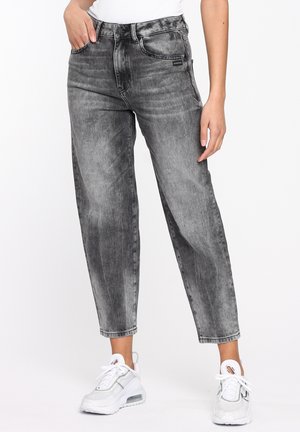 Personne portant un jean droit gris délavé taille haute avec poches avant et des baskets blanches de sport sur fond blanc.