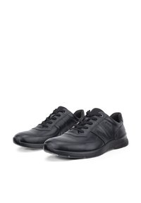 Een paar zwarte lage veterschoenen voor vrijetijd met gestructureerde zolen en gevoerde kraag, afgebeeld op een witte achtergrond.