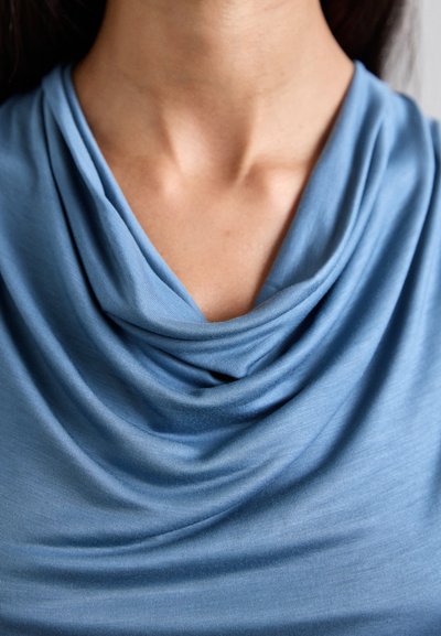 Blå cowl-neck topp gjord av mjukt, lättviktigt tyg. Har draperade veck och en slät textur, med en avslappnad passform runt halsringningen.