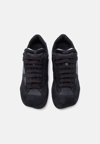 Chaussures de sport noires en mélange de suède et matériaux synthétiques, dotées de lacets plats, d'une surface texturée et d'un design profil bas.