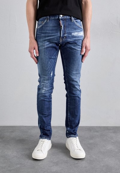Modré slim-fit džíny z denimu s vybledlým designem, obsahující opotřebované detaily a zapínání na knoflík, doplněné o bílé tenisky.