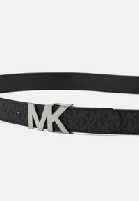 Čierny opasok s logom MK zo strieborného kovu. Obsahuje vzorovanú látkovú časť a hladké kožené akcenty. Nastaviteľná veľkosť s viacerými dierkami.