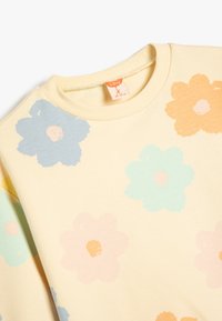 Sudadera de color amarillo claro con un patrón floral en azul, rosa y naranja. Cuello acanalado y textura suave. Etiqueta de la marca visible.