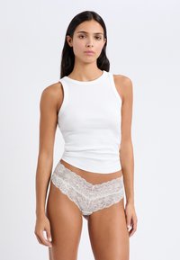 Weißes, geripptes Tanktop, kombiniert mit Unterwäsche aus leichtem Material mit Spitzenrand. Glattes Gewebe mit figurbetontem Schnitt und subtiler Textur.