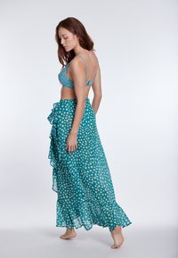 Bikini zgornji del v teal barvi s pikicami in tankimi naramnicami, v kombinaciji z usklajenim, rahlo padajočim maksi krilom z ruffles in visokim razporkom.