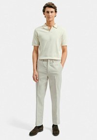 Ljusbeige polo med krage och subtil kontrastkant, parat med ljusgrå skräddarsydda byxor och mörkbruna mockaskor.